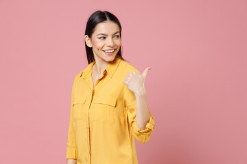 Young brunette smiling cheerful nice happy cute latin happy attractive cute woman 20s in yellow shirt point hands aside on copy space area mock up isolated on pastel pink background studio portrait.