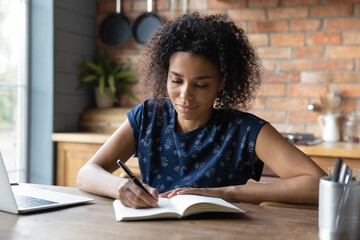 Self education. Busy african woman remote student learn from home on distance take short written notes. Interested black teen female watch video lesson tutorial online on pc write in copybook by hand
