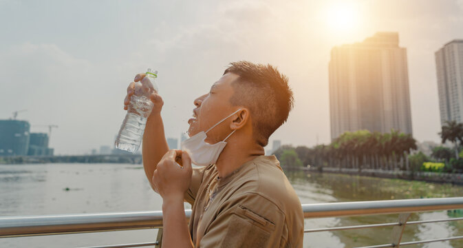 Young asian runner man putting off face mask while using water in bottle to wash his face after finished running and working out.