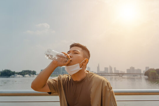 Young asian runner man putting off face mask while drinking water after finished running and working out. He wearing medical mask