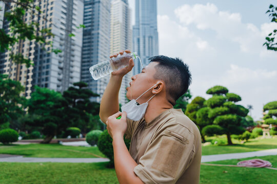 Young asian runner man putting off face mask while using water in bottle to wash his face after finished running and working out.