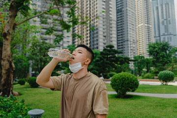Fototapeta premium Young asian runner man putting off face mask while drinking water after finished running and working out. He wearing medical mask
