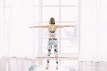 beautiful attractive cute athletic woman blonde with a slim figure does sports yoga exercises supports leads a healthy lifestyle at home in the morning in the afternoon on the opposite window 