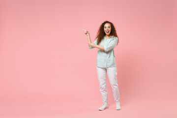 Fototapeta na wymiar Full length young black african happy smiling friendly curly woman 20s wearing blue casual shirt standing point index finger aside on workspace area isolated on pastel pink background studio portrait.