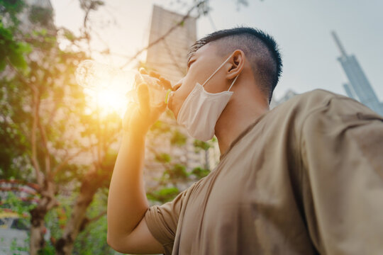Young asian runner man putting off face mask while drinking water after finished running and working out. He wearing medical mask - Powered by Adobe