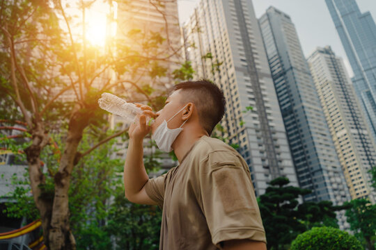 Young asian runner man putting off face mask while drinking water after finished running and working out. He wearing medical mask