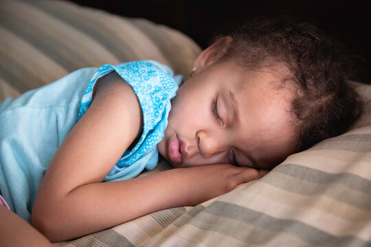 Toddler girl cuddled up and sleeping peacefully on a large bed surrounded by crumpled sheets