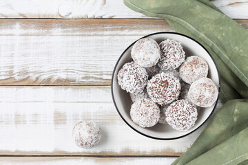Obraz na płótnie Canvas Coconut energy balls in a white cup on a light wooden background. Top view.