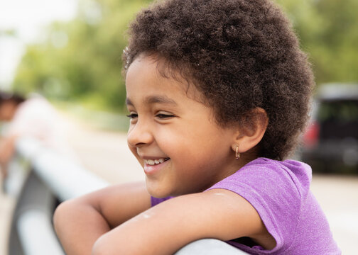 Pretty girl with short curly kinky hair leaning on a fence rail and smiling happily