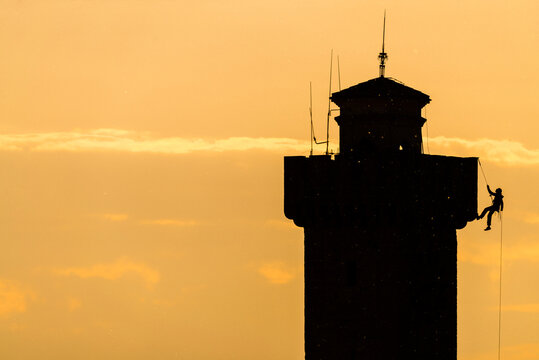 Alpinist hanging on rope near tower against sunset