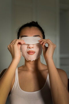 Portraiture of a young asian woman putting on a moisturised face-mask