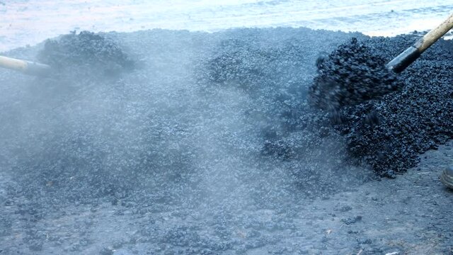 Heavy industry workers in uniform throw hot asphalt on road. Work with shovels. Repair new bitumen