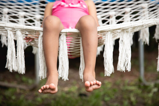 Closeup of a pretty toddler child's toes as she sits happily in a crochet yarn hammock.