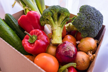 Set of different fresh vegetables in a cardboard box. Home delivery of groceries during coronavirus quarantine. Broccoli, leek, cucumbers, bell peppers, tomatos, onions bought in a supermarket.