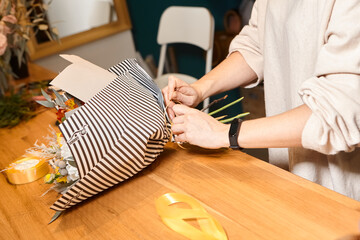 Florist works with colors. Flower seller chooses flowers for future bouquet. Flowers shop worker in a mask standing in flower shop and checking flowers in glass vase.