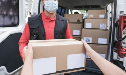Woman receiving package from delivery man - Young man wearing surgical face mask at work for coronavirus outbreak