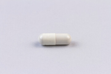 One white medicine capsule on the grey background