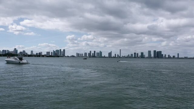 A luxury yacht and a speeding jet ski cross, Miami Florida skyline, storm clouds on the horizon