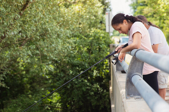 Portrait of a teen girl peering over a ledge as she and her grandfather fishes