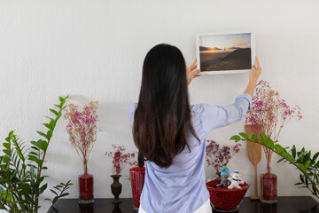 young asian woman hanging a picture in her home
