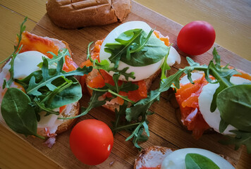 Poached egg on grilled toast with smoked salmon, rucola and vegetables on white board. healthy breakfast