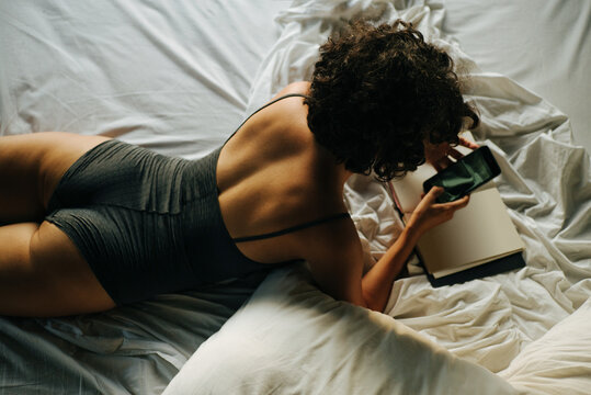 Beautiful curly girl in bed with a smartphone
