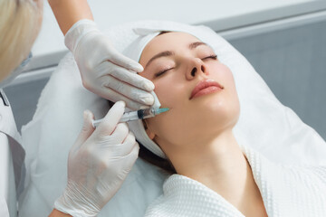 Obraz na płótnie Canvas The doctor cosmetologist makes the rejuvenating facial injections procedure for tightening and smoothing wrinkles on the face skin of a beautiful, young woman in a beauty salon. Cosmetology, skincare