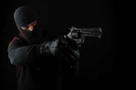 Man wearing balaclava holding pistol, standing shooting with a gun, isolated on black background.