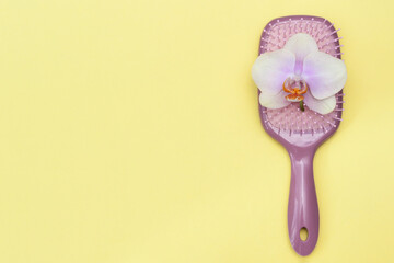 Massage hair brush with orchid flower on yellow background, flat lay, copy space.