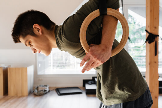 Young man exercising on rings with effort