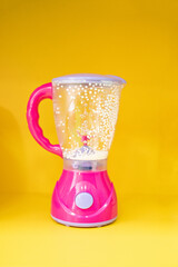 small toy pink blender on a yellow background.