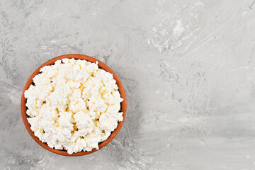 Soft curd natural healthy food, wholesome diet food. Homemade cottage cheese in a clay bowl on a gray neutral background, top view with copy space.