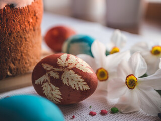 Stylish easter eggs natural dyed and homemade easter cake on rustic cloth with flowers on wooden table. Happy Easter. Traditional Easter food.