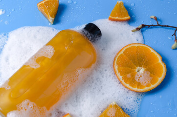 Shampoo, gel, liquid soap of orange color from natural ingredients in a transparent bottle on a blue background in soapy foam with orange pieces, flat lay copy space