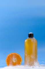 Shampoo, gel, liquid soap of orange color from natural ingredients in a transparent bottle stands on a blue background in soapy foam with orange pieces, vertical background, copy space