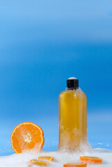 Obraz premium Shampoo, gel, liquid soap of orange color from natural ingredients in a transparent bottle stands on a blue background in soapy foam with orange pieces, vertical background, copy space
