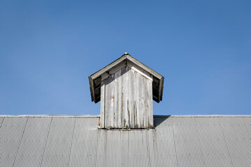Old Wood Cupola on a Barn Roof of Corrugated Metal under a Clear Blue Sky