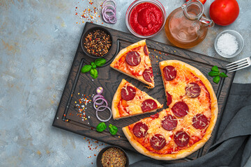 Pizza with salami on a gray background with ingredients.