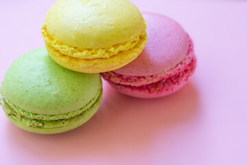 Close up view of pink, yellow and green macaroons french traditional cookies made of almond flour. Sugary biscuits on pink background