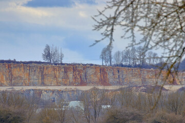stone pit with a cloudy sky behind parts of a bare tree
