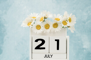 White cube calendar for july decorated with daisy flowers on blue