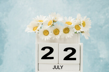 White cube calendar for july decorated with daisy flowers on blue