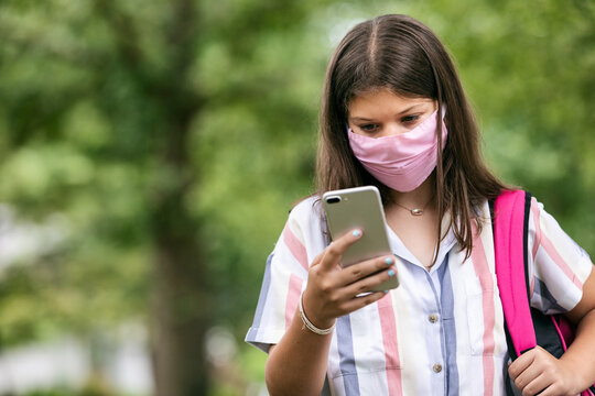 Student: Teen Girl With Face Mask Looks At Phone On Way To Schoo