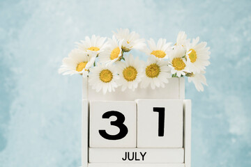 White cube calendar for july decorated with daisy flowers over blue with copy space