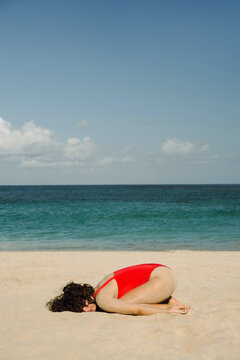 A curly girl in a red bathing suit lies on the beach.