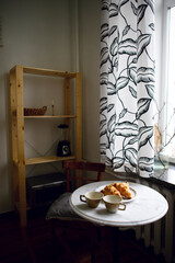 coffee with croissants on the kitchen table by the window. morning coffee ritual. fresh pastries and coffee. cozy interior