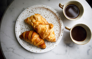 two cups of black coffee with fresh croissants on a white marble table. morning coffee ritual. wonderful breakfast