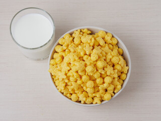 Tasty corn flakes in bowl with bottle of milk. Rustic wooden background with homespun napkin. Healthy crispy breakfast snack. Place for text. Top view, flat lay.