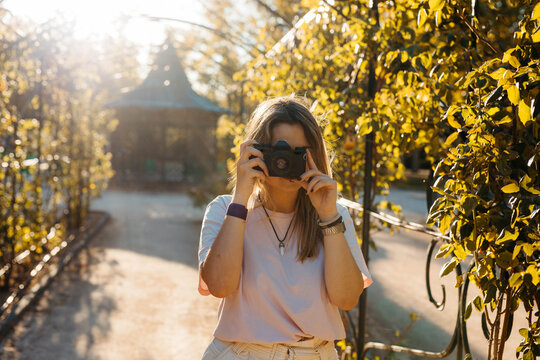 Curvy blonde girl taking photos in a park with an analog camera. He wears a pink shirt.