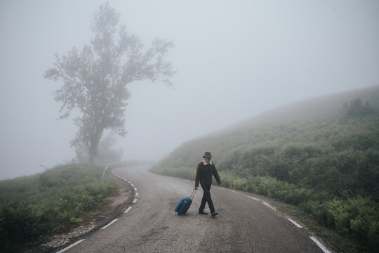 a man with luggage on an empty rural road